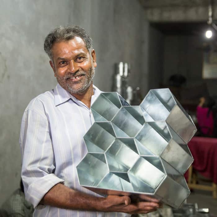 A man holding up a metal tray in a fair trade factory.
