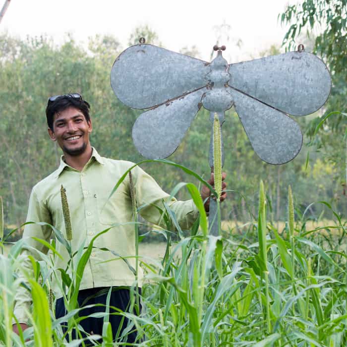 A man practicing fair trade by showcasing a metal dragonfly in a field.