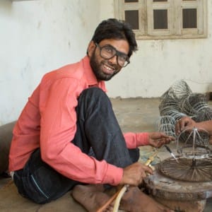 Intizar Hussain observing two men working on a wire wheel in a workshop.