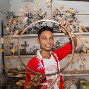 A man, Kamrul Hasan, holding up a metal wreath in a shop.