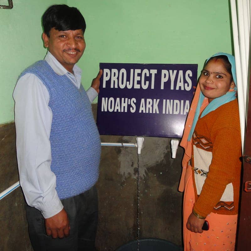 A man and woman standing next to the Project Pyas sign in India.