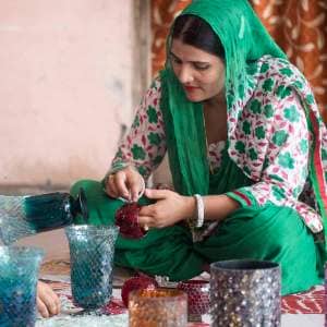 A woman in a green sari, Mohammad Riyaz, is working on a glass vase.