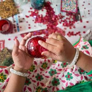 A girl, Mohammad, in a red dress is making a red ornament.