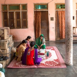 A group of women sitting on a rug in a room, depicted by Mohammad Riyaz's artwork.