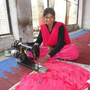 A woman in a pink sari sewing on a machine as part of Project Disha.