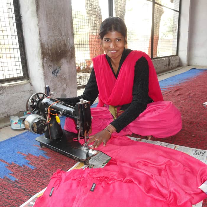 A woman in a pink sari sewing on a machine as part of Project Disha.
