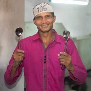 Dilshad Hussain wearing a pink shirt, holding two spoons.