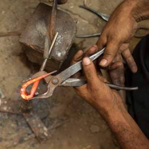 Dilshad Hussain is using pliers to work on metal.