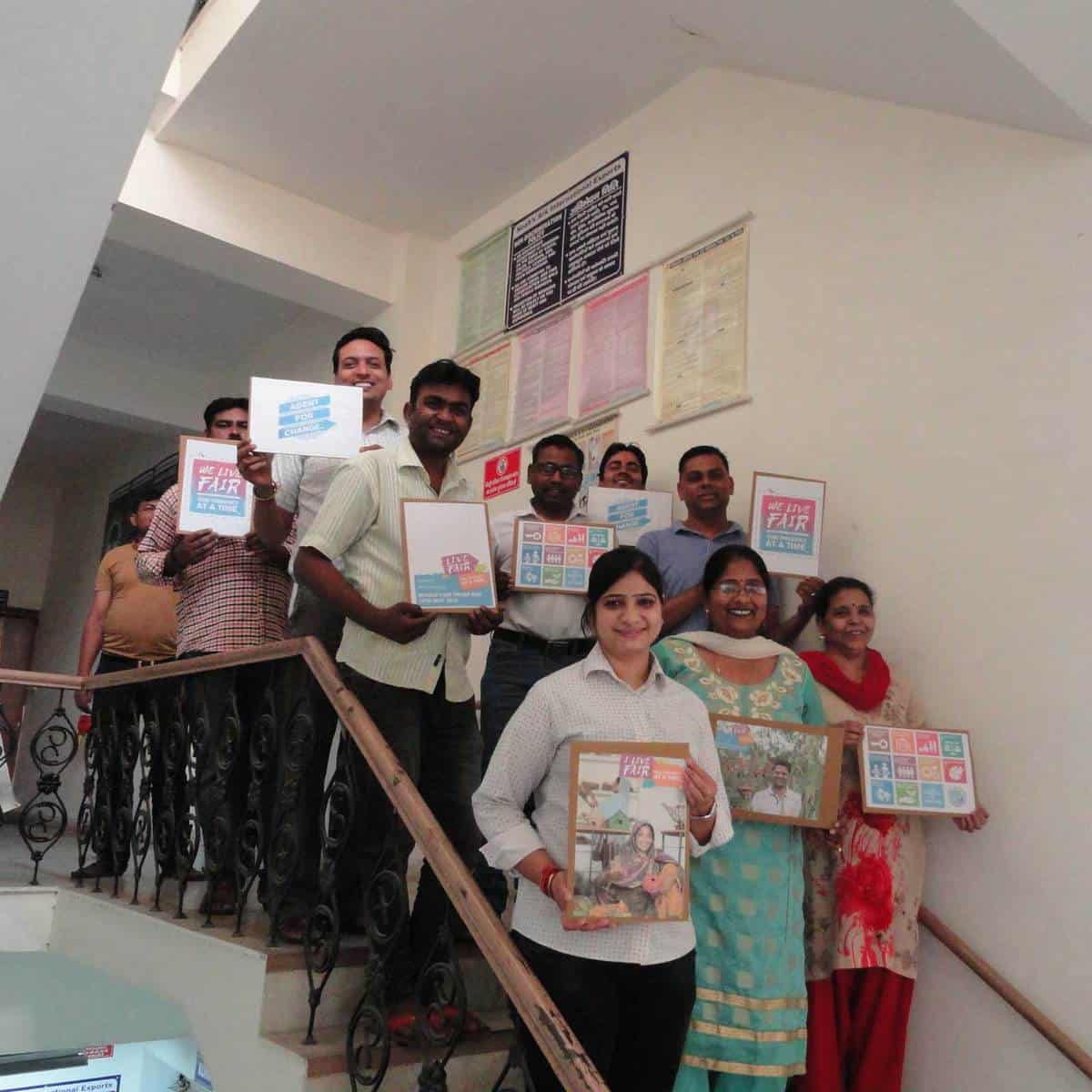 A group of people on a fair trade staircase holding up pictures.