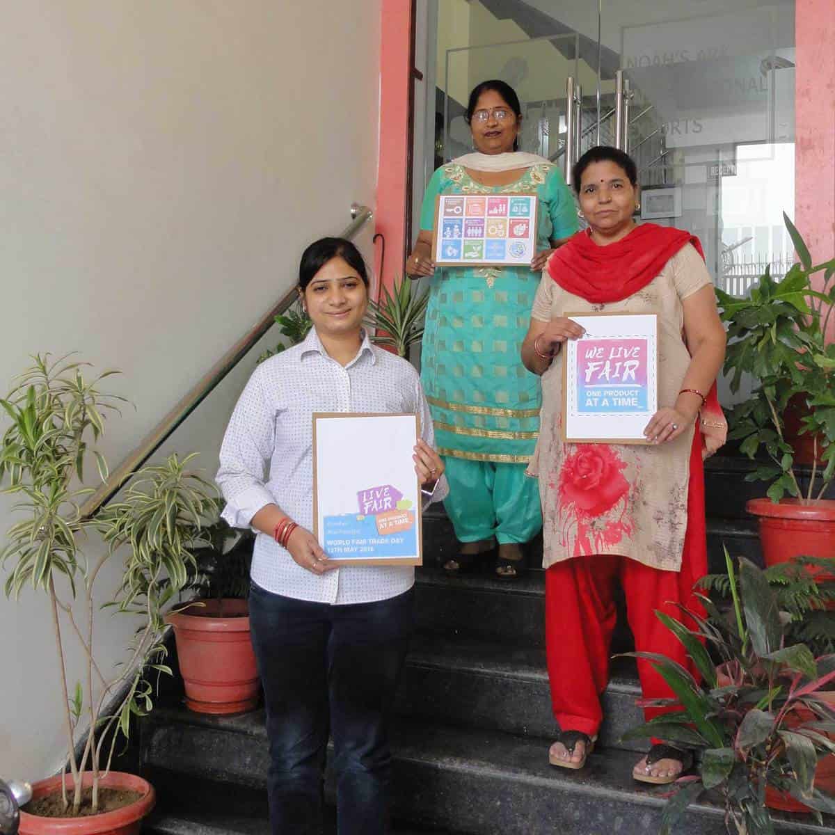 Three women promoting Fair Trade by standing on steps and holding signs.