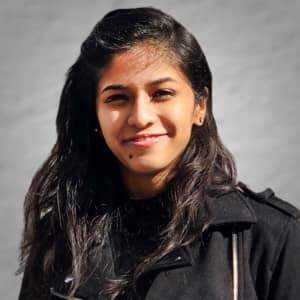 A woman, wearing a black jacket and smiling, poses for Samuel Masih's camera.