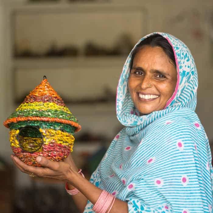A woman in a sari holding a colorful birdhouse, inspired by Intizar Hussain.
