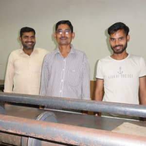 Three men standing in front of a box making machine.